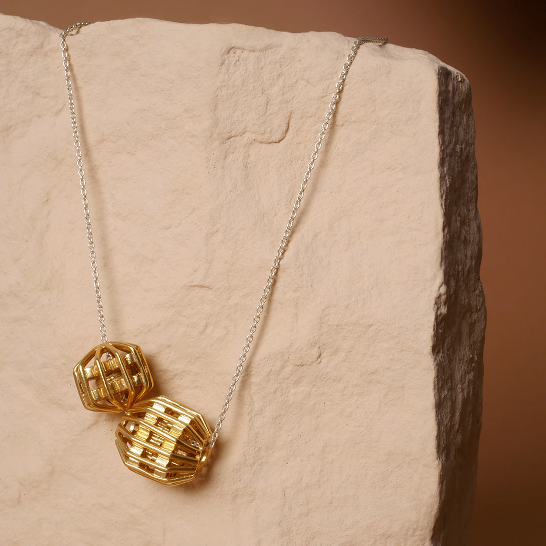 Collar con cadena de plata y dijes geométricos dorados tipo globo, diseño artesanal de Mariana Shuk sobre piedra color arena.