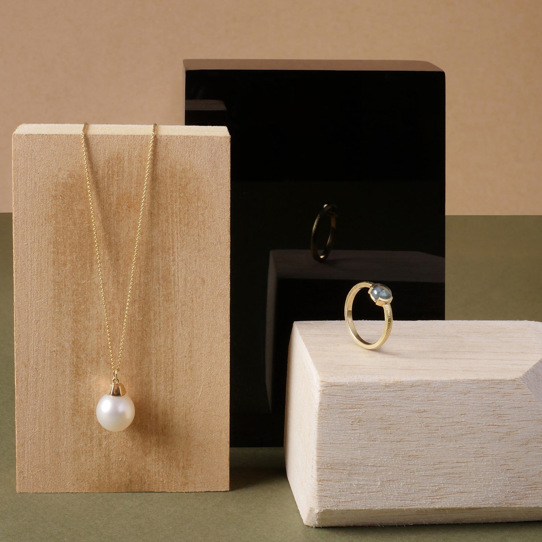 Collar con perla natural de 13 mm y anillo con zafiro montaña en oro amarillo 18k, diseño artesanal de Mariana Shuk sobre bloques de madera.  Select 75 more words to run Humanizer.