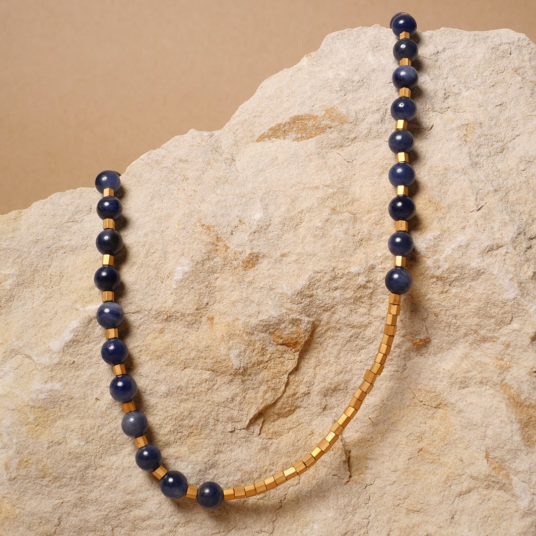 Collar artesanal con cuentas de lapislázuli de 6 mm y cubos dorados, diseño contemporáneo de Mariana Shuk sobre piedra natural beige.