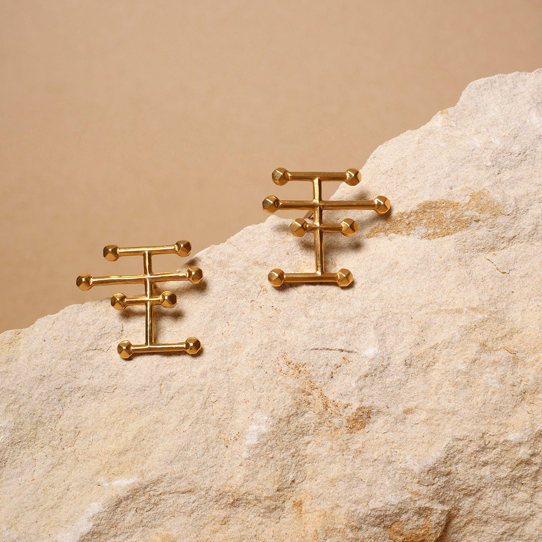 Aretes Taches mini en plata, con enchape de oro amarillo, foto ambientada con piedra. Joyería de autor, hecho en Colombia por Mariana Shuk.