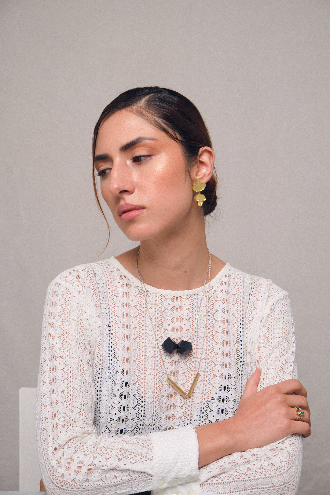 Foto de  modelo con aretes hojas espejo en plata y acrílico, color dorado, cadena dijes tubos, cadena dije poliedro y anillo balance con esmeralda y diamantes. Joyería de autor, hecho en Colombia por Mariana Shuk.