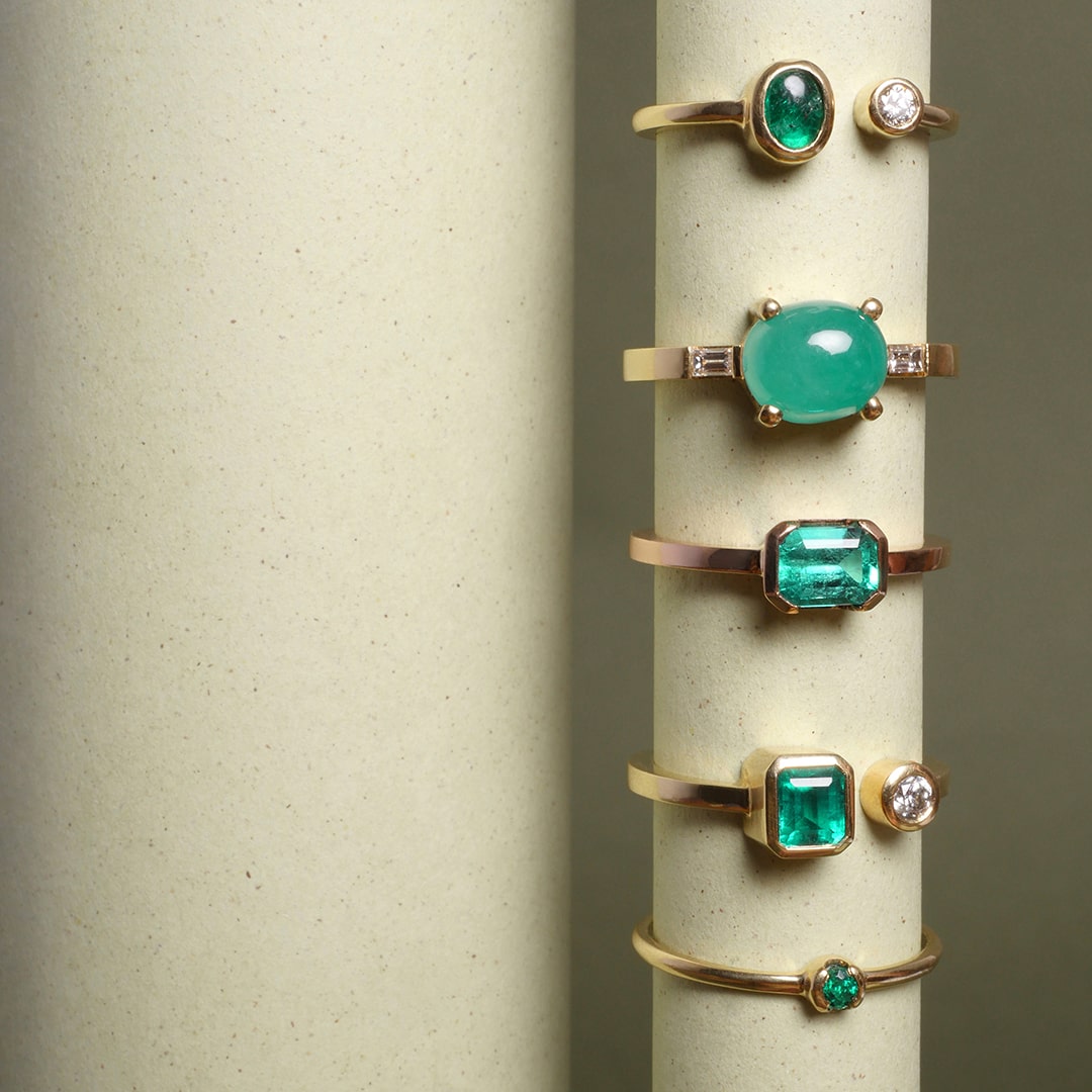 Anillos con esmeraldas colombianas en oro amarillo de 18k, diseño artesanal de alta joyería por Mariana Shuk. Foto de papel sobre fondo beige.