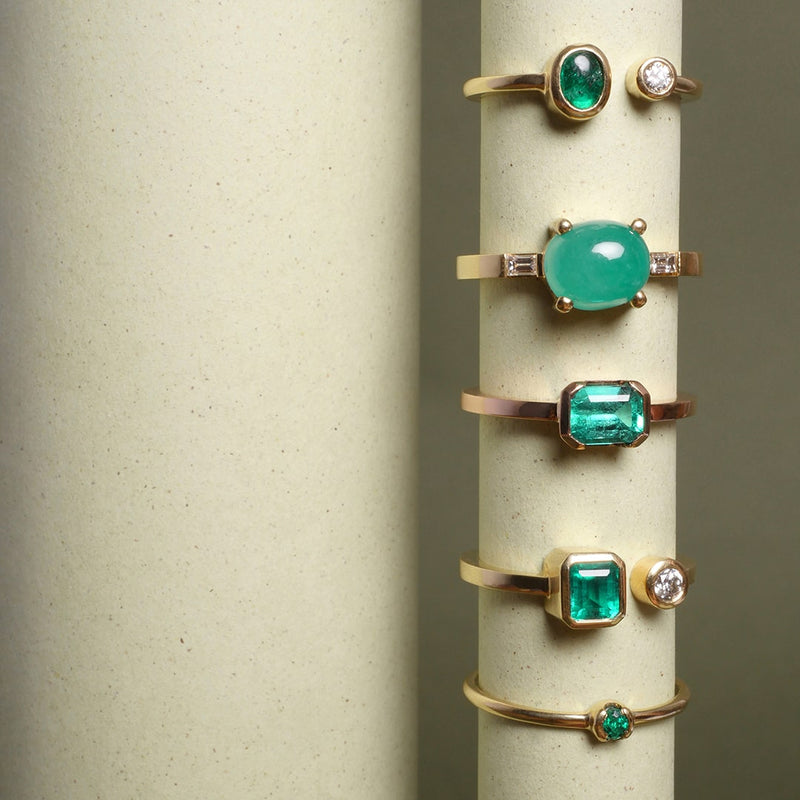Anillos con esmeraldas colombianas en oro amarillo de 18k, diseño artesanal de alta joyería por Mariana Shuk. Foto de papel sobre fondo beige.