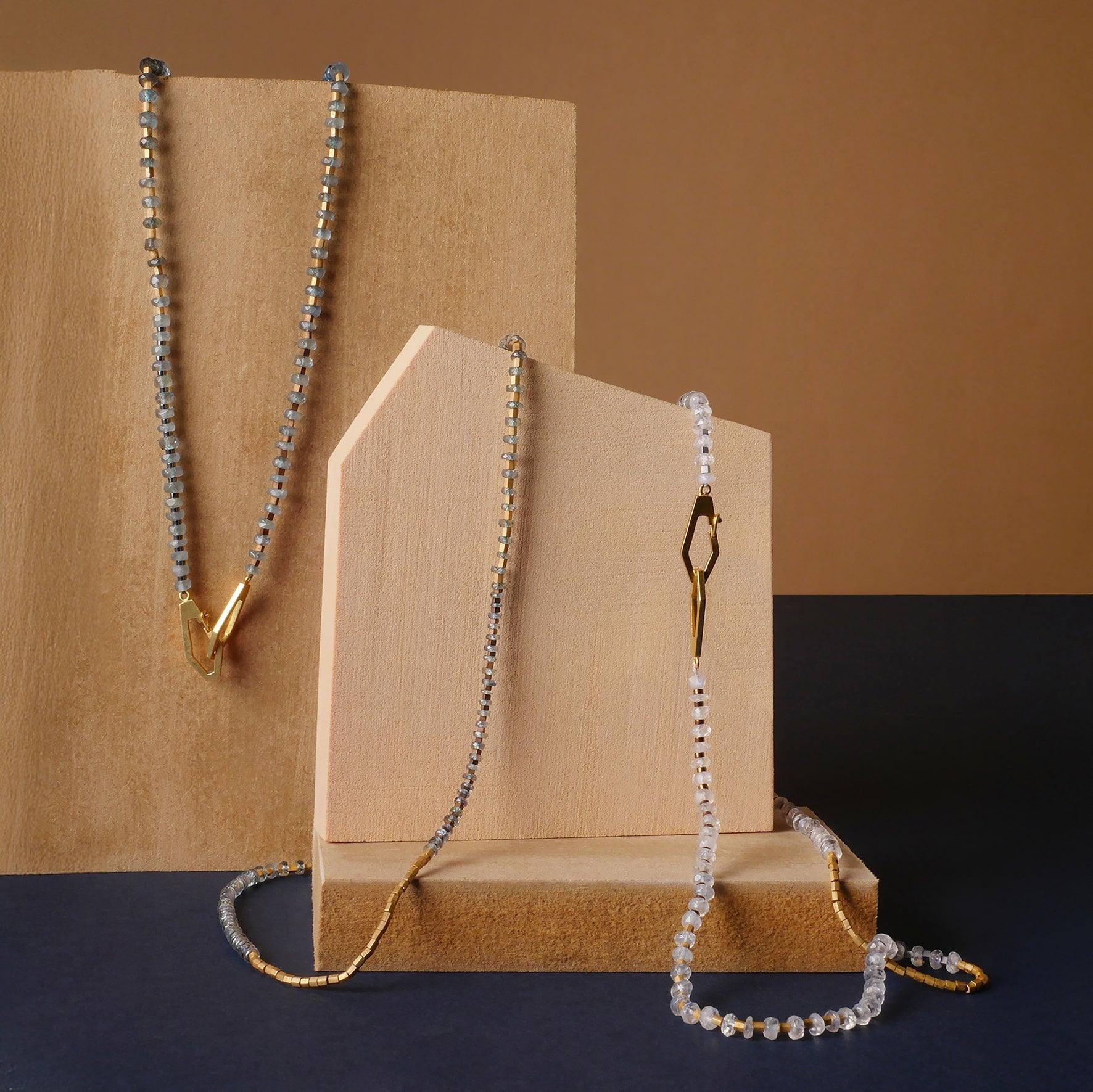 Collares con cuentas de piedra luna arcoíris y zafiro verde, detalles en oro de Mariana Shuk, diseño artesanal sobre fondos de madera.