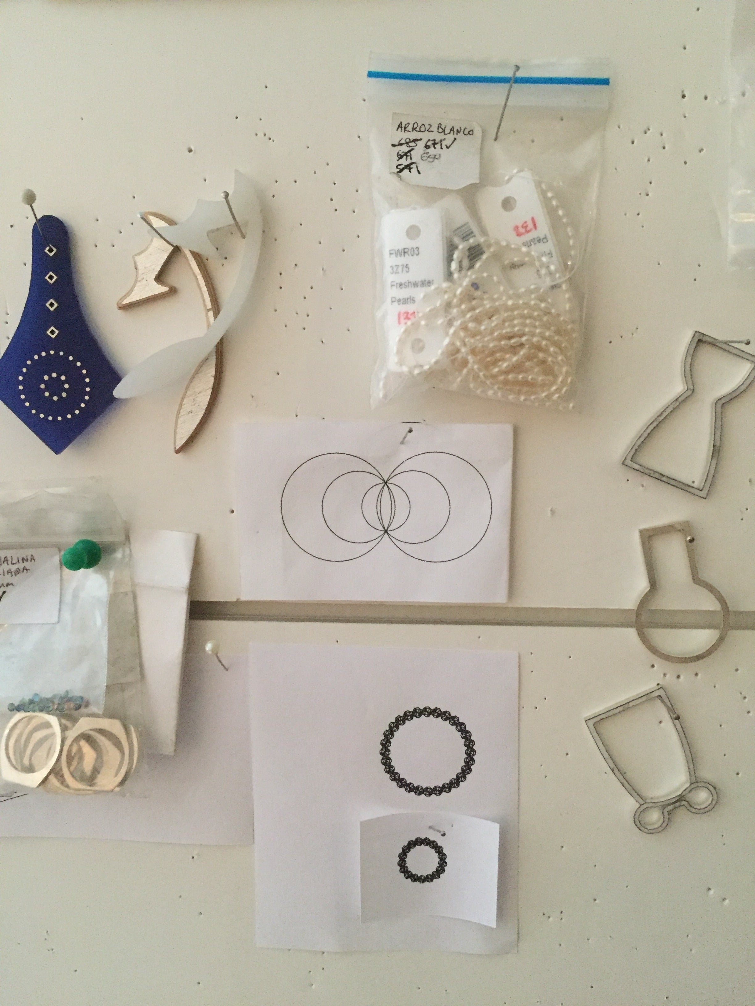Cartelera de diseño de producto en el taller de Mariana Shuk con bocetos de joyería, moldes en plata y acrílico, perlas cultivadas y elementos de proceso artesanal.