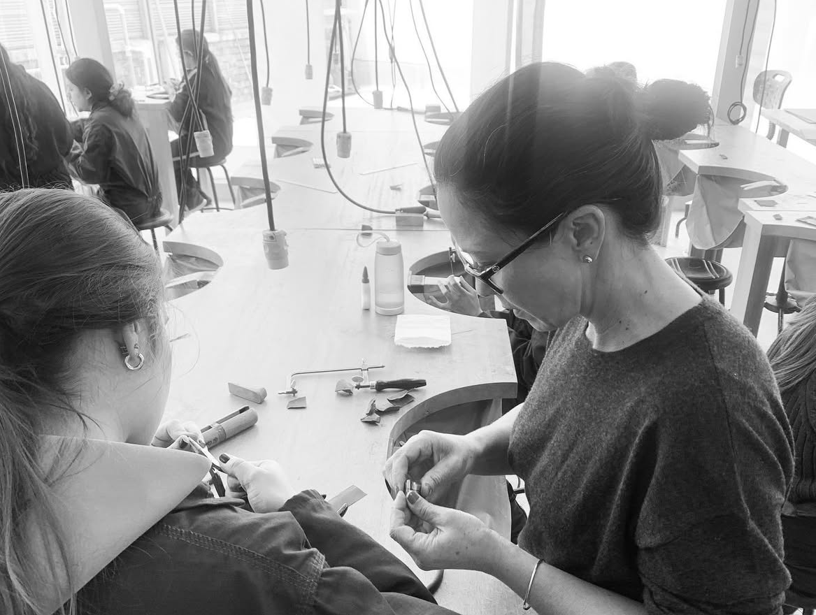 Mariana Shuk enseñando diseño de producto y técnicas de joyería artesanal en su taller, guiando a una estudiante durante el proceso de creación.