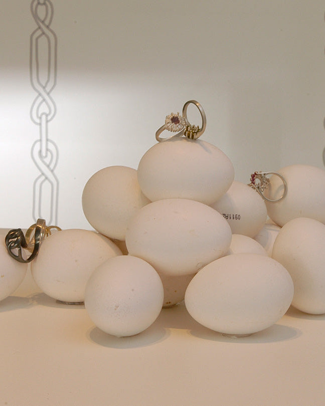 Montaje artístico de diseño de producto de Mariana Shuk con anillos de joyería artesanal en plata y oro exhibidos sobre formas escultóricas blancas.