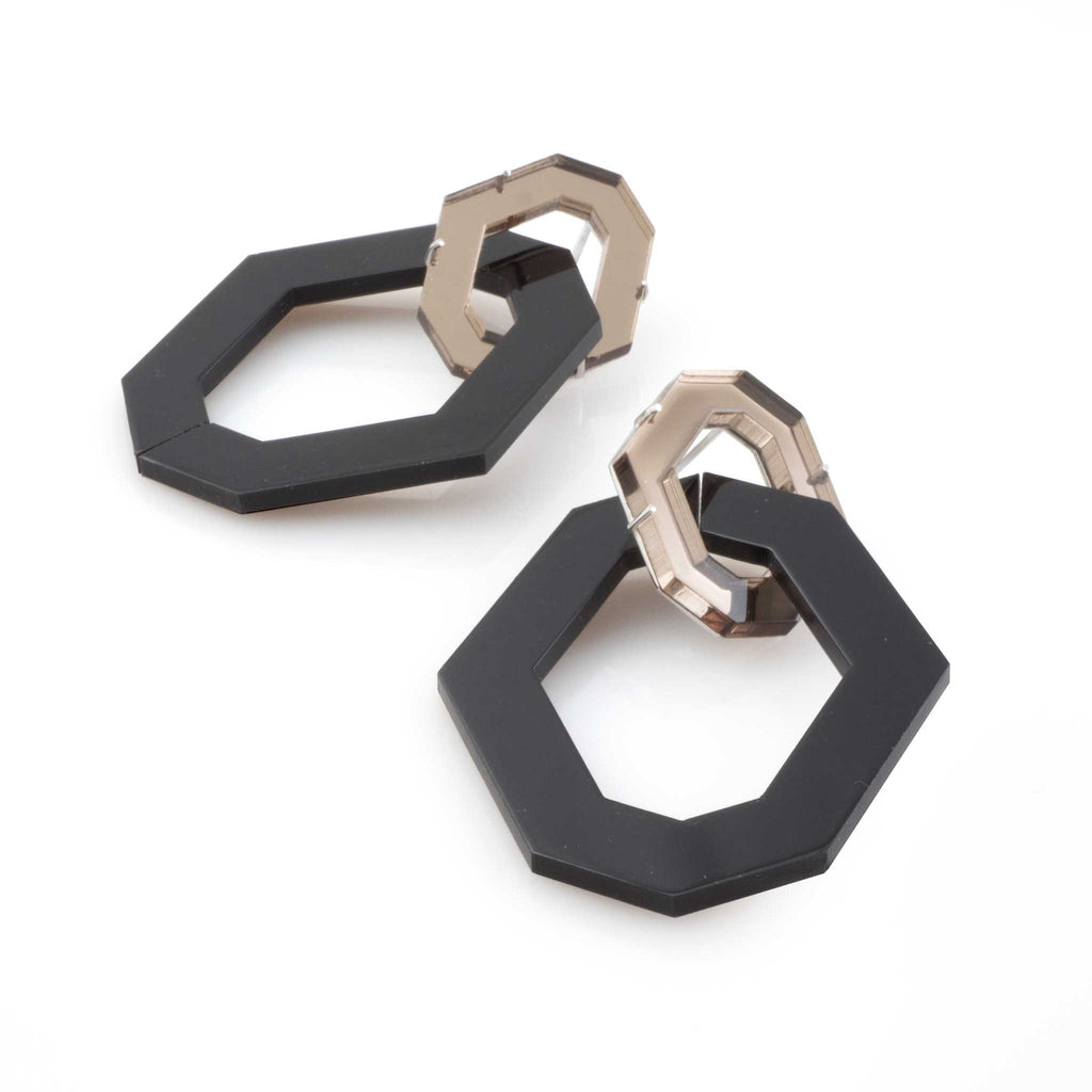 Aretes dos hexágonos en acrílico esmerilado negro y acrílico espejado bronce, foto con vista frontal. Joyería artesanal inspirada en naturaleza y geometría. Diseños exclusivos, hecho en Colombia por Mariana Shuk.