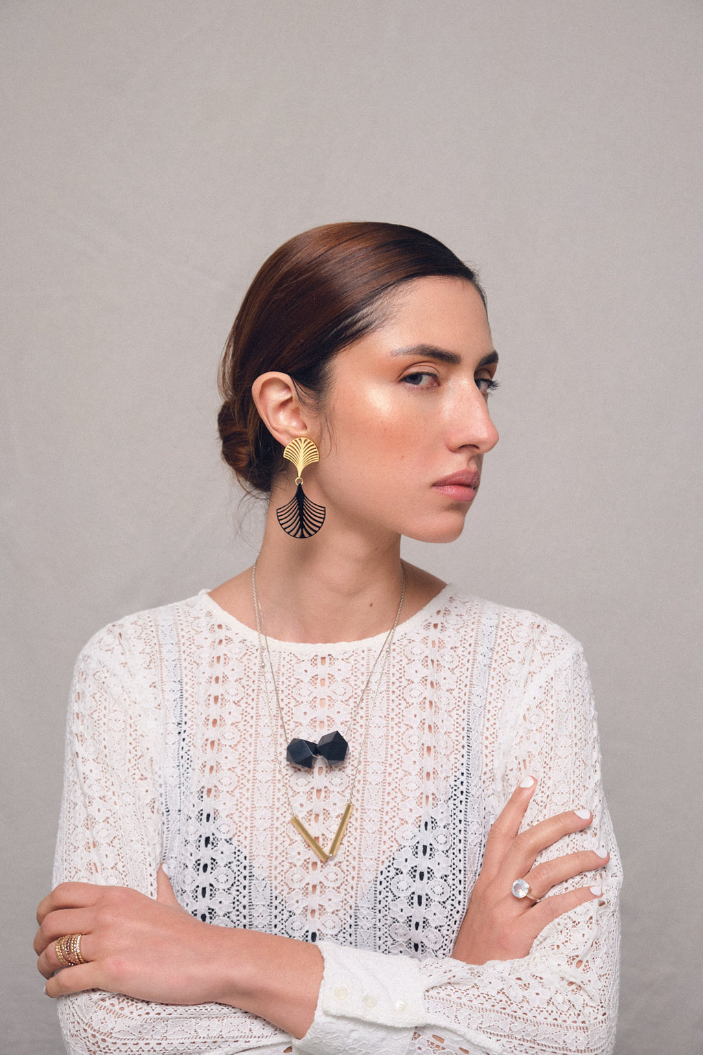 Pendientes Palma Deco, collar dos poliedros acrílico, collar con dije tubos, foto con modelo de lejos. Joyería hecha a mano que combina elegancia minimalista y estructura. Diseños exclusivos, hecho en Colombia por Mariana Shuk.